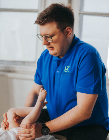 Fizjoterapeuta Łukasz Kusowski ćwiczący z niemowlakiem na łóżku do fizjoterapii