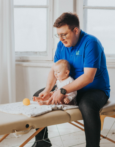 Fizjoterapeuta Łukasz Kusowski ćwiczący z niemowlakiem na łóżku do fizjoterapii