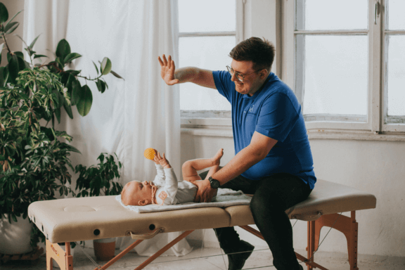 Fizjoterapeuta Łukasz Kusowski ćwiczący z niemowlakiem na łóżku do fizjoterapii