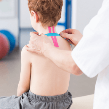 fizjoterapeuta naklejający tapy na plecy małego chłopca